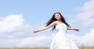 beautiful young brunette woman outdoor on the hill on a summer day, against blue sky with clouds