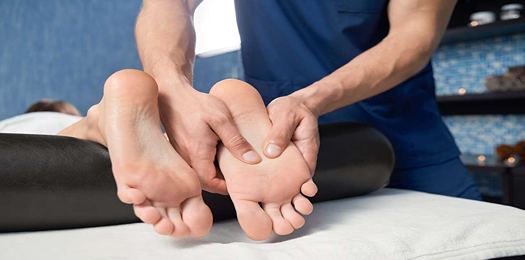 Closeup of hands of qualified masseur massaging foot of female client in spa cosmetology salon. Woman lying on couch, relaxing and enjoying during healthy procedure. Concept of body care.