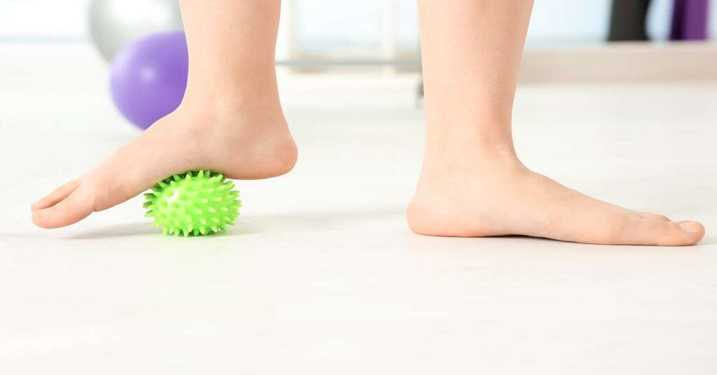 Feet of woman doing exercises with rubber ball in clinic